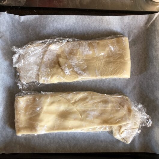 two folded, covered wonton wrapper dough resting on parchment-lined pan