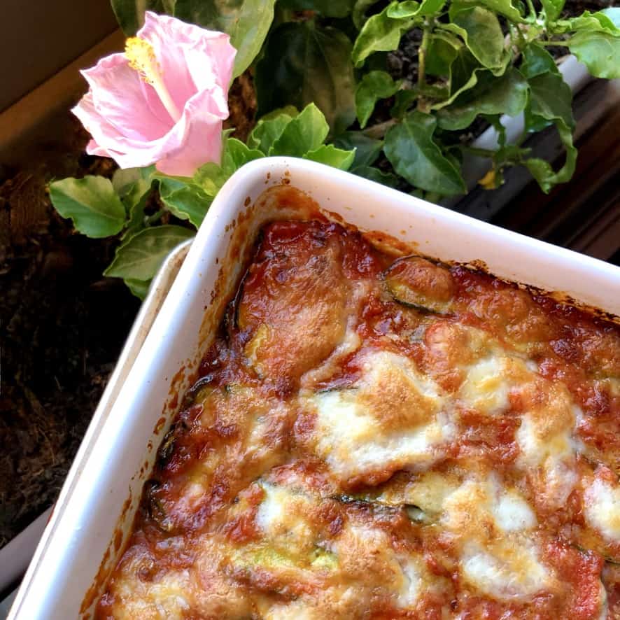 a closeup of a corner of the parmigiana after being baked with a pink flower growing in the window box planter just behind it