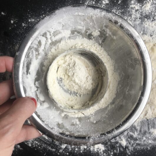 a round cookie cutter in a bowl of flour to dust it before cutting the dough