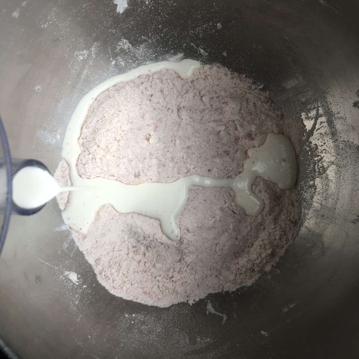 pink strawberry scone mixture with heavy cream being added into the bowl