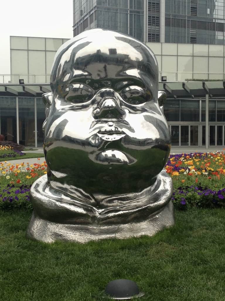 Giant Silver Buddha head sculpture on top of a rooftop garden