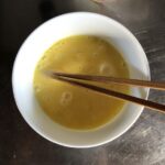 beaten eggs in a white bowl with chopsticks resting in it