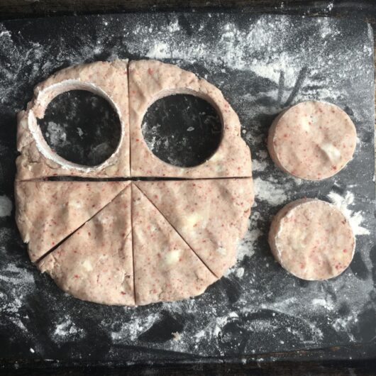two round cutouts taken from the strawberry scone dough from the top half of the disc while the bottom half of the disc has been sliced into pie wedge shapes