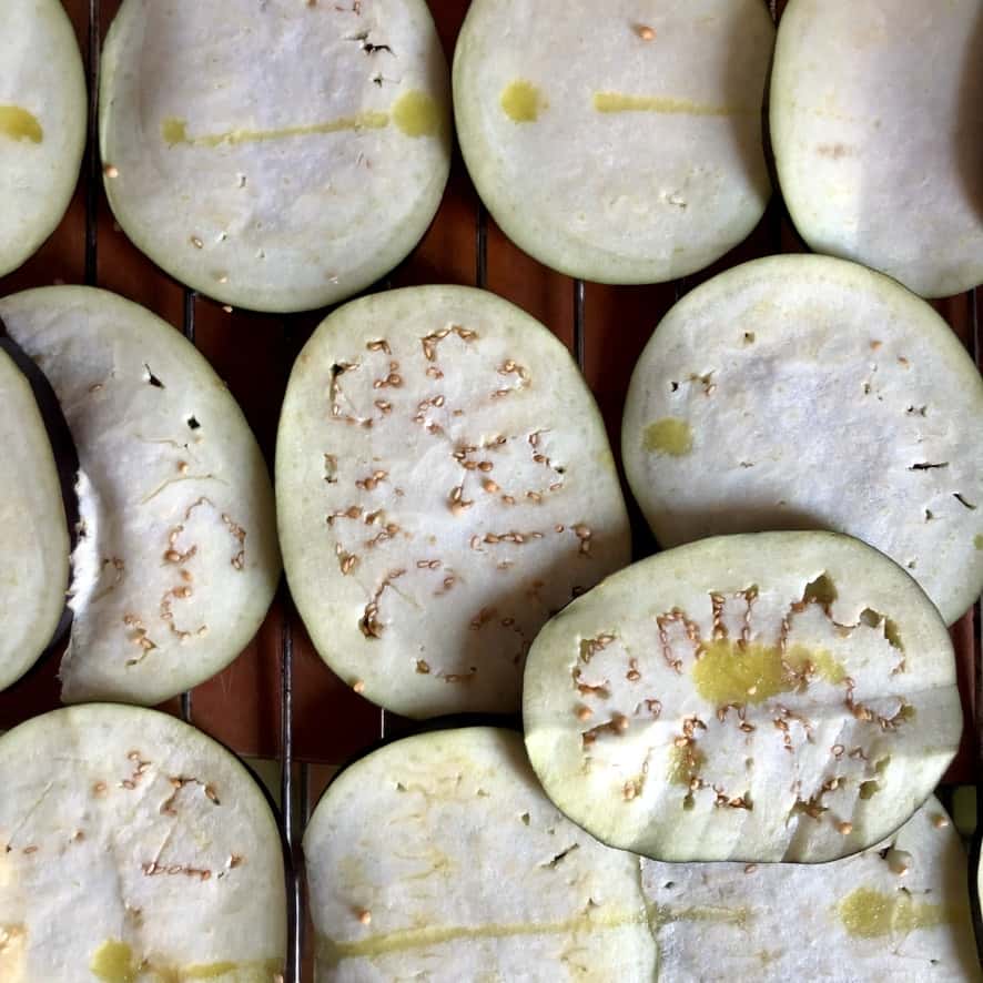 thinly sliced eggplant rounds on a wire oven rack drizzled with olive oil and sprinkled with salt