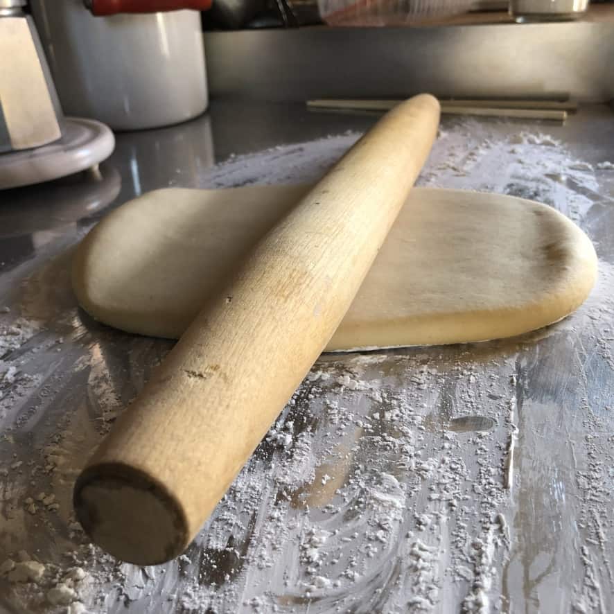 A rolling pin in the middle of the soft wonton disc being rolled out.