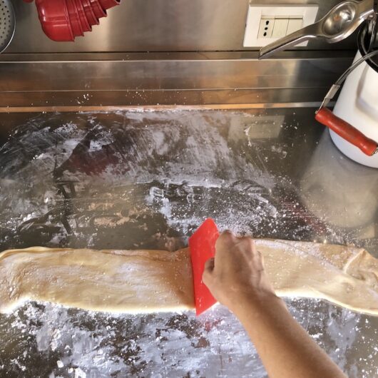 my hand dividing the rested wonton dough with the red dough cutter
