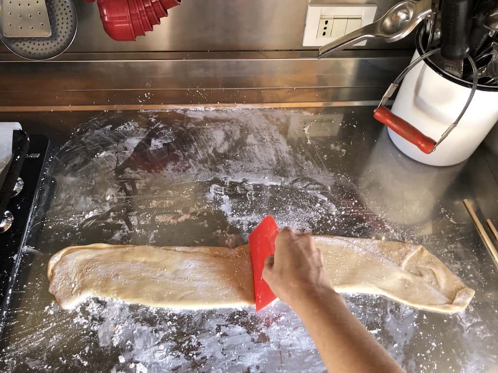 my hand dividing the rested wonton dough with the red dough cutter