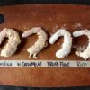 four Argentinian Red Shrimp dusted each with a different type of flour or cornmeal on an Epicurean Cutting board and a line of masking tape below the lined up shrimp indicating what has been used on each shrimp in the lineup