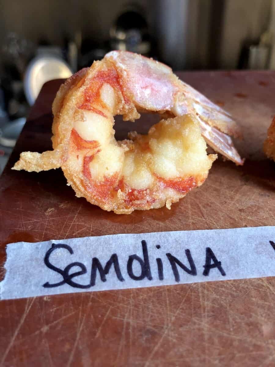 single fried shrimp with masking tape on the cutting board in front of it with black sharpied "Semolina" written on it