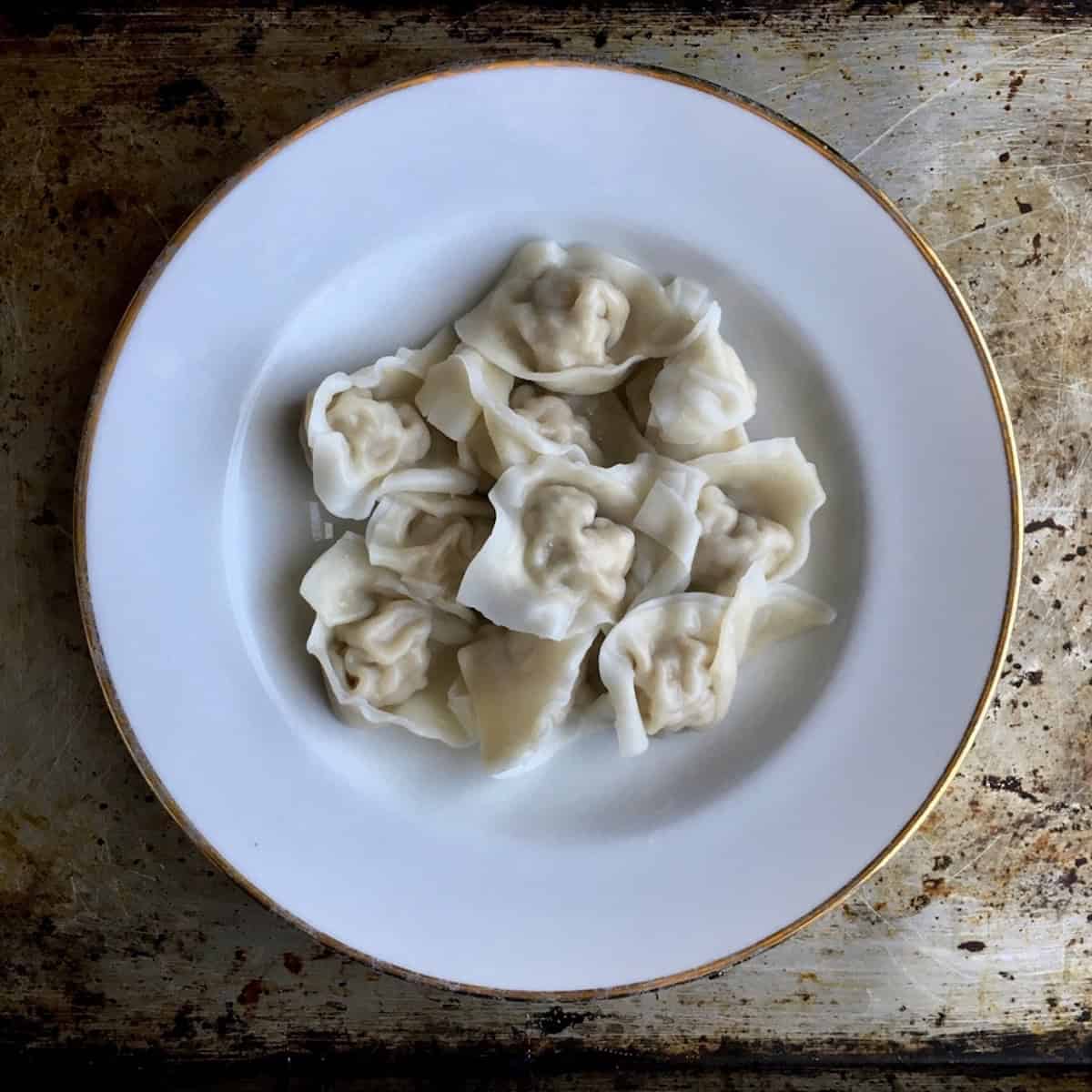 
Homemade boiled Sichuan pork wontons in a wide shallow bowl ready for chili oil, pork wonton recipe made with homemade wonton wrappers.
