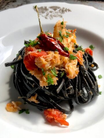 Crab linguine with black squid ink pasta in bowl garnished with chives and sauteed spicy red pepper, squid ink pasta with crab recipe.