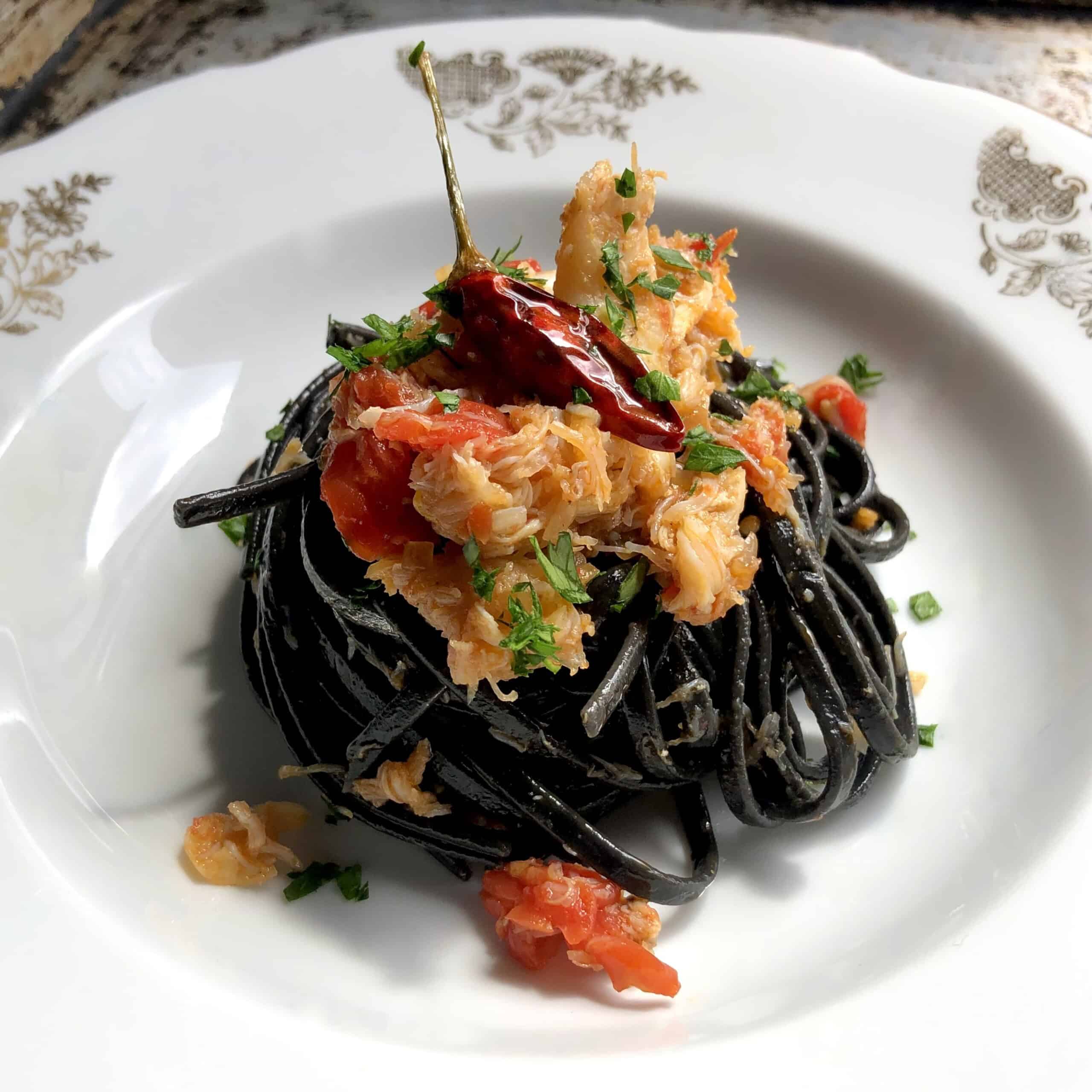 Crab linguine with black squid ink pasta in bowl garnished with chives and sauteed spicy red pepper, squid ink pasta with crab recipe.