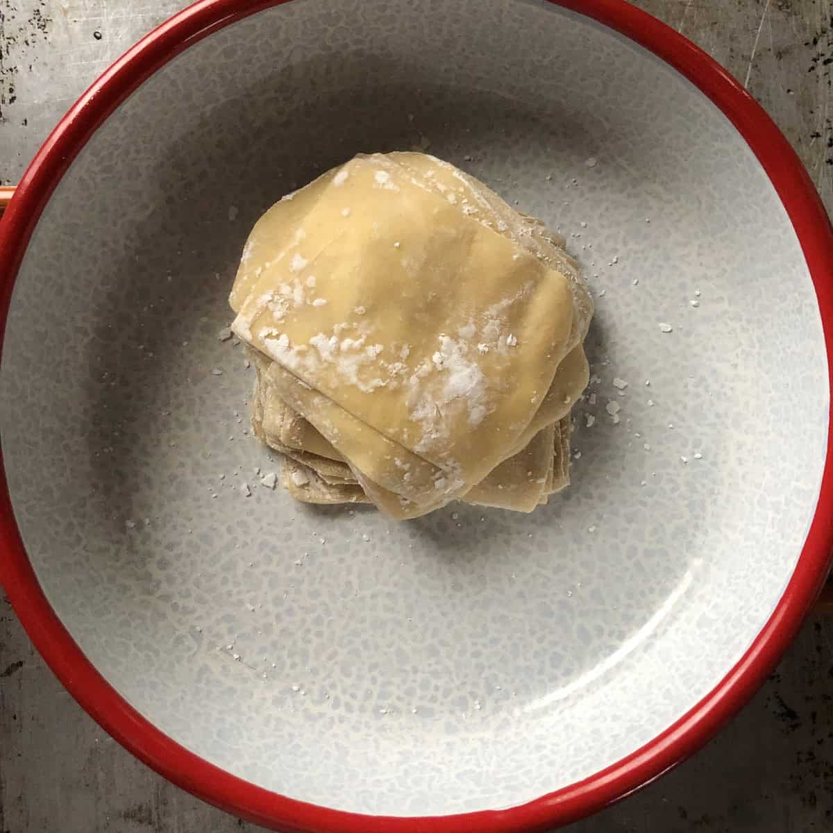 A stack of previously frozen homemade wonton wrappers thawed overnight in the fridge showing how perfectly they hold up after freezing.
