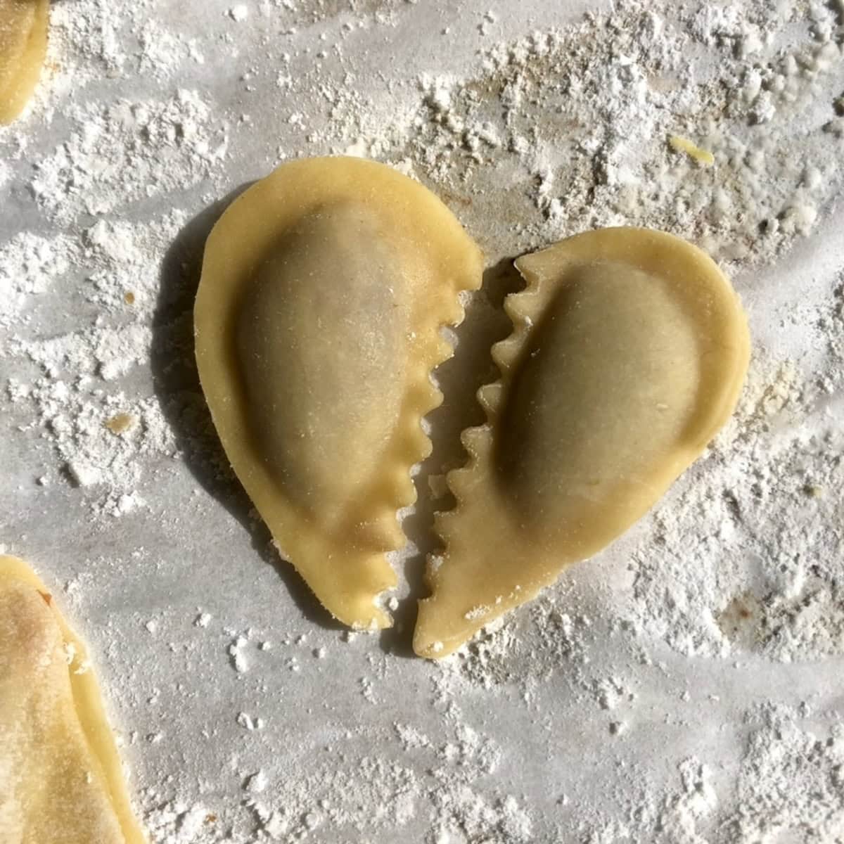 Broken heart-shaped homemade wontons with pork and ginger filling, each half cut with a zigzag center and filled separately using wonton wrapper dough from scratch.

