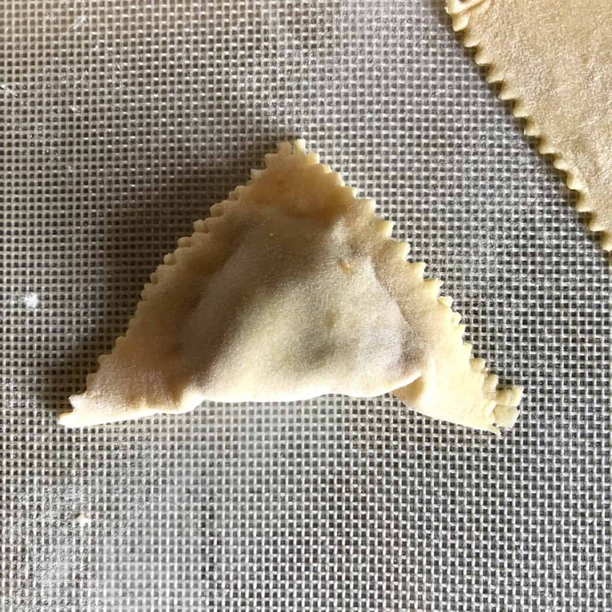 A wonton with pork filling folded into a triangle and sealed by pinching the edges closed, how to fold wontons step by step with homemade wonton wrappers.
