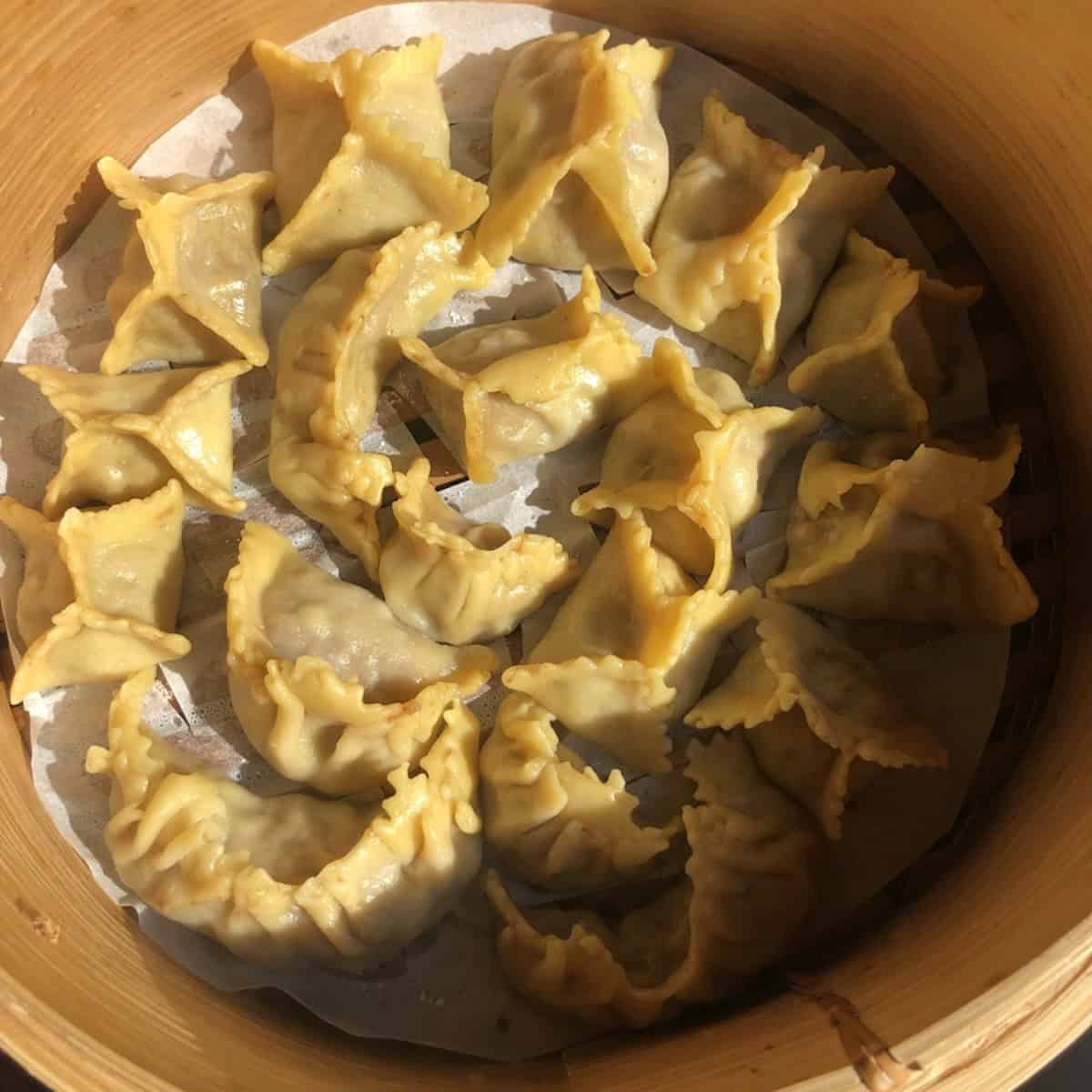 Shaped wontons steaming in a parchment-lined bamboo steamer, how to make wontons steamed with homemade wonton wrappers.

