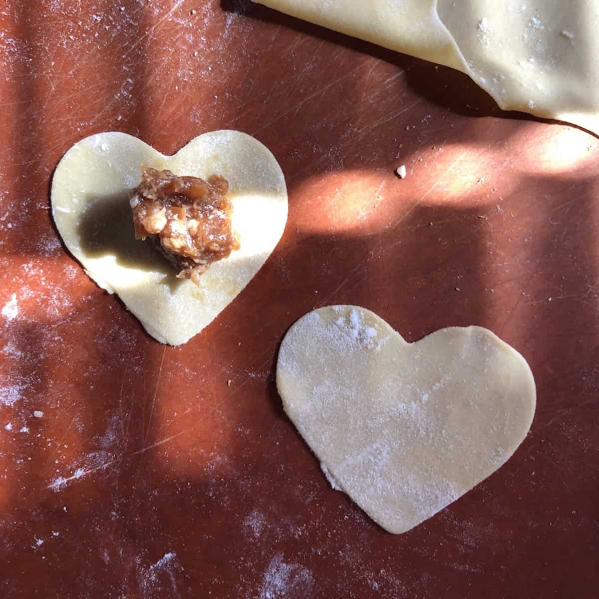 Heart-shaped wonton wrapper with Sichuan pork filling in the center and another heart-shaped dough ready to seal on top, pork wonton recipe with homemade wonton wrappers.