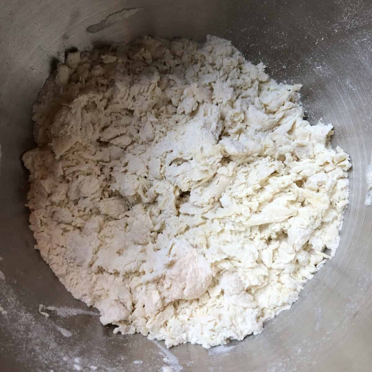 Shaggy wonton wrapper dough with eggs mixed into the flour in a mixing bowl ready for water, what are wonton wrappers made of step by step.

