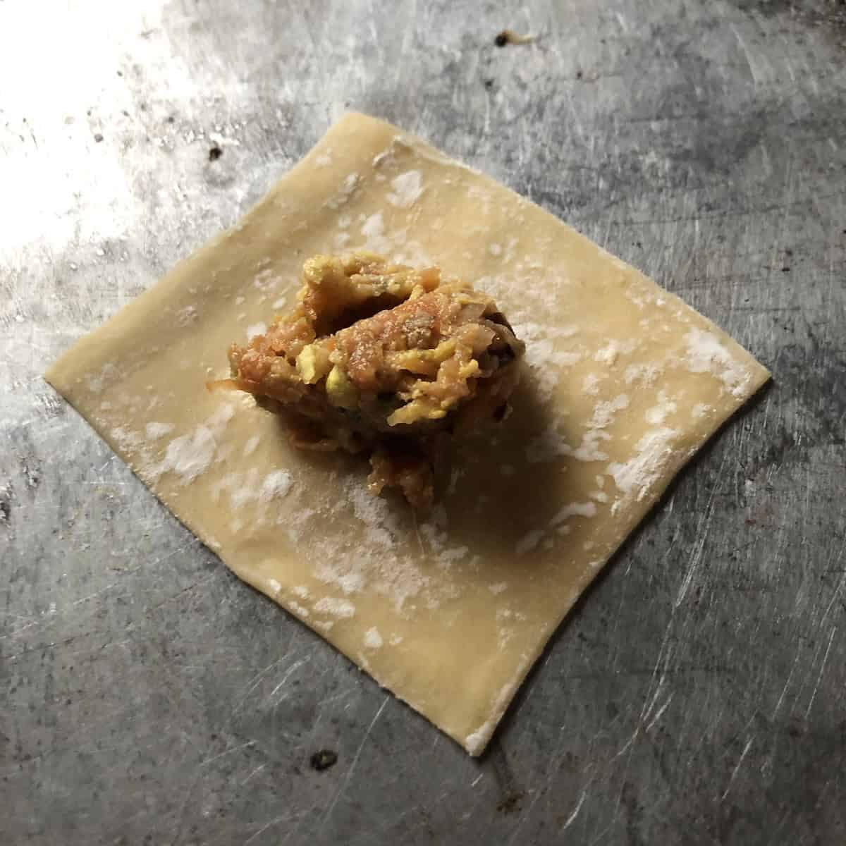 Homemade wonton wrapper with a pork and mushroom wonton filling added to the center ready to fold.
