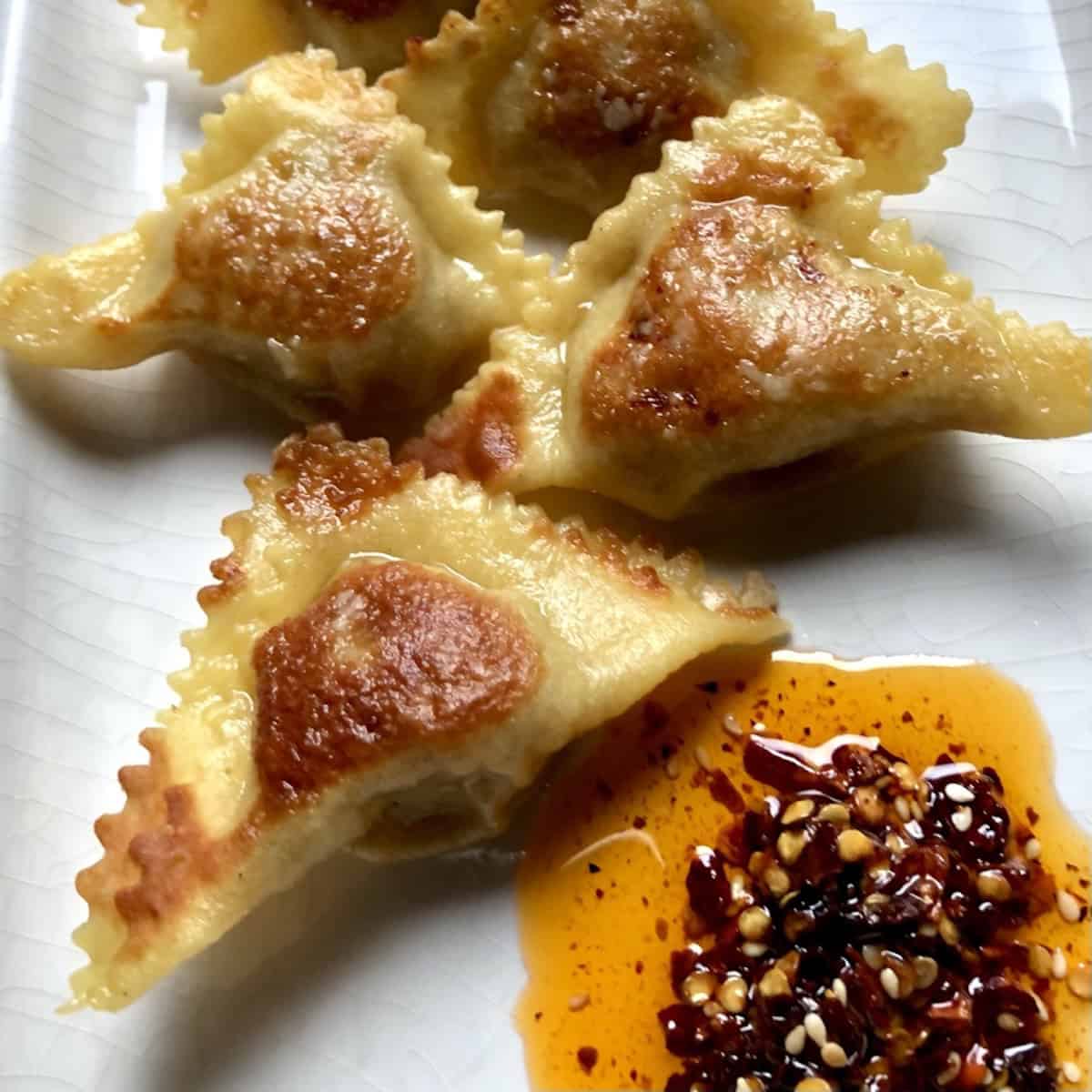 Pan-fried shaped wontons with crisp golden edges in a dark skillet made with homemade wonton wrappers, crispy wonton recipe cooked until golden brown.
