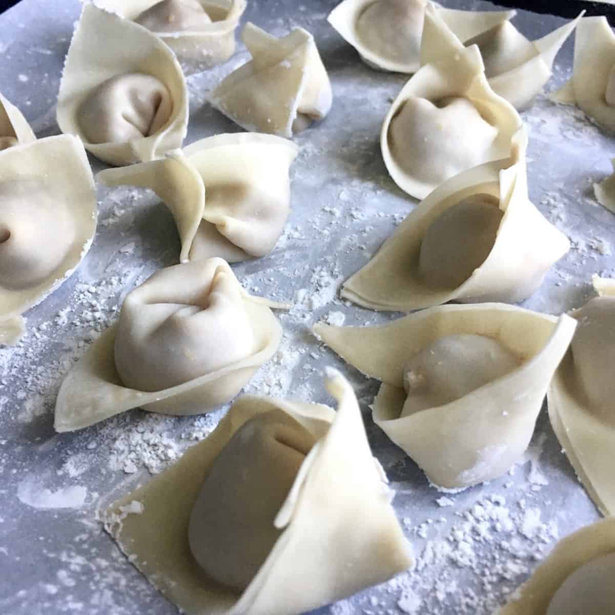 A traditional folded and shaped wonton with pork wonton filling ready to cook, how to make wontons with homemade wonton wrappers.
