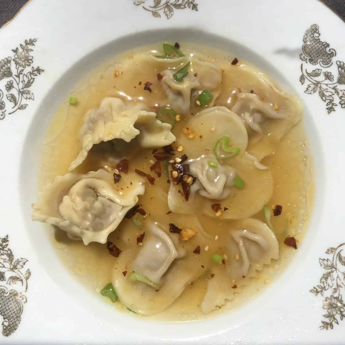 Homemade wonton soup with Sichuan pork and ginger filling in heart-shaped, traditional, and dumpling purse-style wontons in a Chinese wonton soup broth.