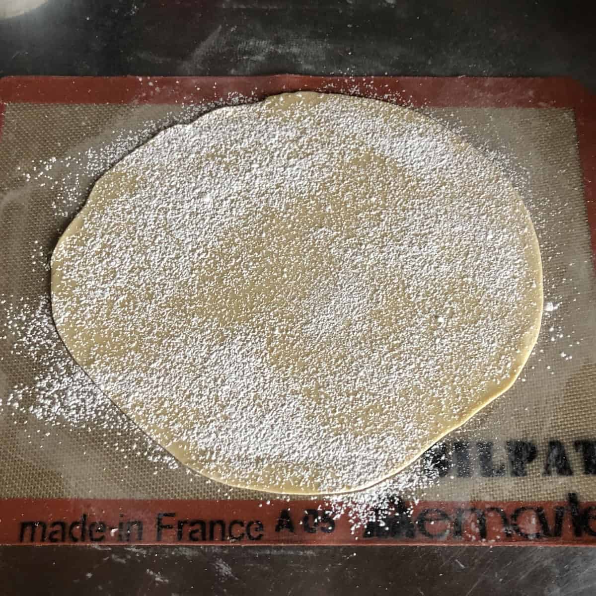 Wonton wrapper dough rolled out to a quarter inch on a cornstarch-dusted Silpat sprinkled with more cornstarch and ready to fold, what are wonton wrappers made of and how to roll them thin.

