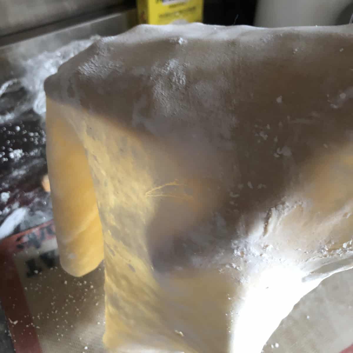 Hand holding up properly rolled wonton wrapper dough with light shining through to show the ideal one-eighth inch thickness, wonton wrappers recipe for thin homemade wonton skins.

