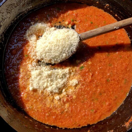 red sauce with cream and scallions with a heaping mound of grana padano cheese on a spoon about to be stirred in