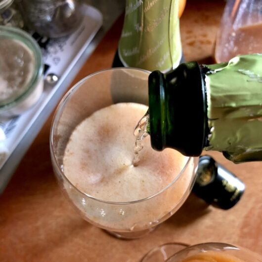 pouring proscecco into a prosecco glass filled with fruit juice