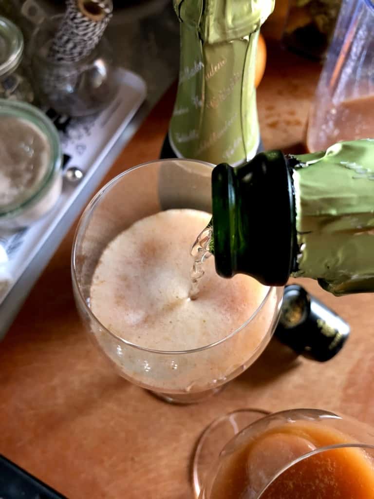 pouring proscecco into a prosecco glass filled with fruit juice