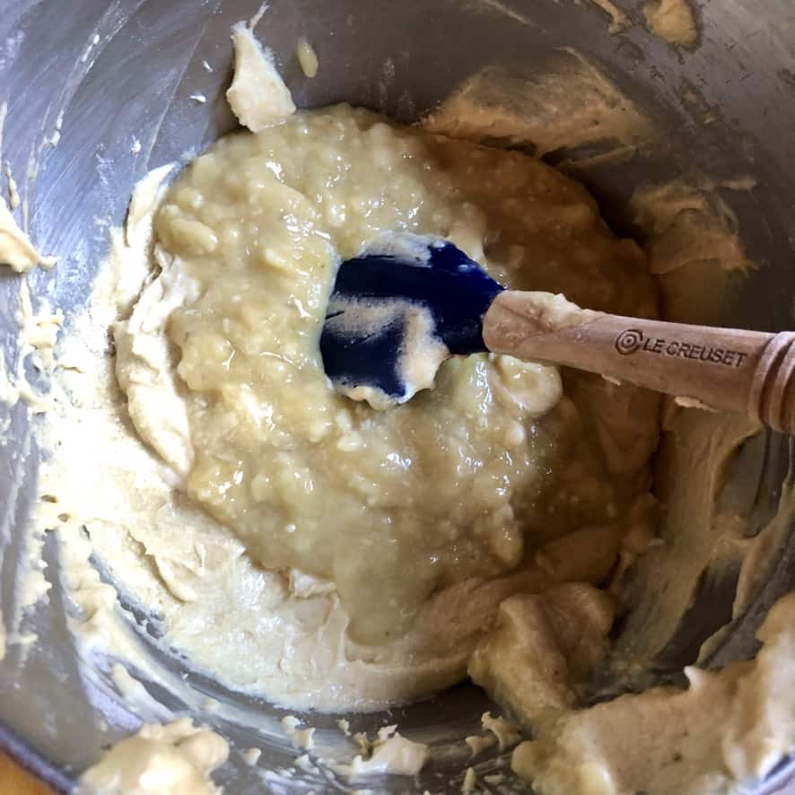 mashed bananas on top of the creamed butter, sugar, and egg mixture with a blue le creuset rubber spatula in the bowl