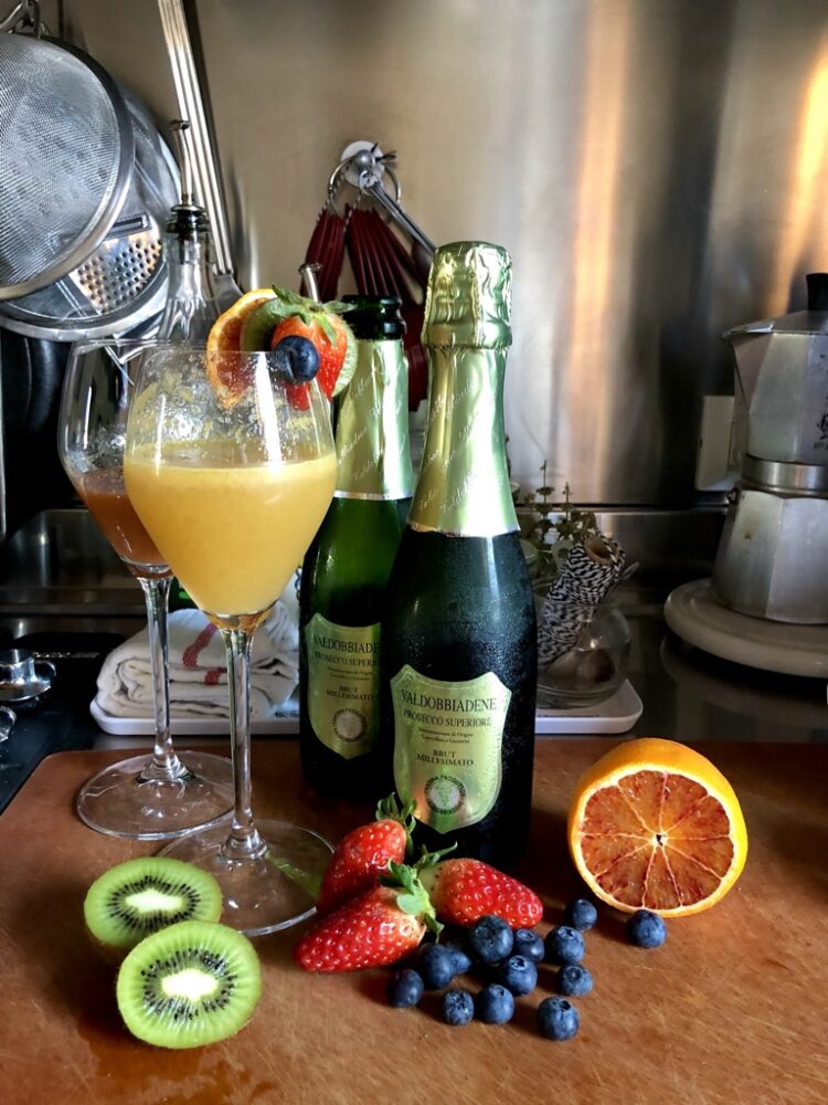 bellinis in prosecco glasses with bottles of prosecco and fruit around the feet of the glasses