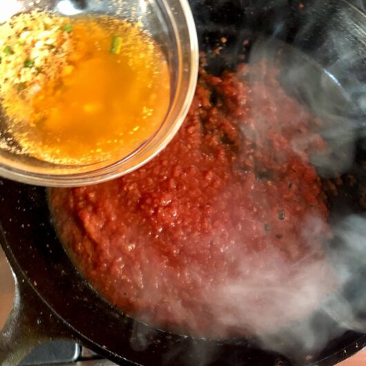 pouring clarified shrimp butter into the tomato sauce
