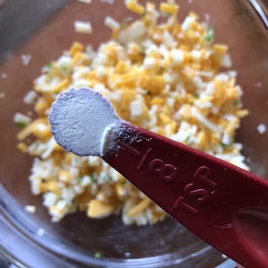 measuring spoon with small amount of flour held over the diced cheese bowl
