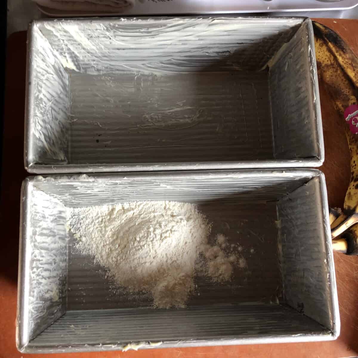 Two Buttered loaf pans with one of them containing a little flour that will be shaken around to coat the pan fully.