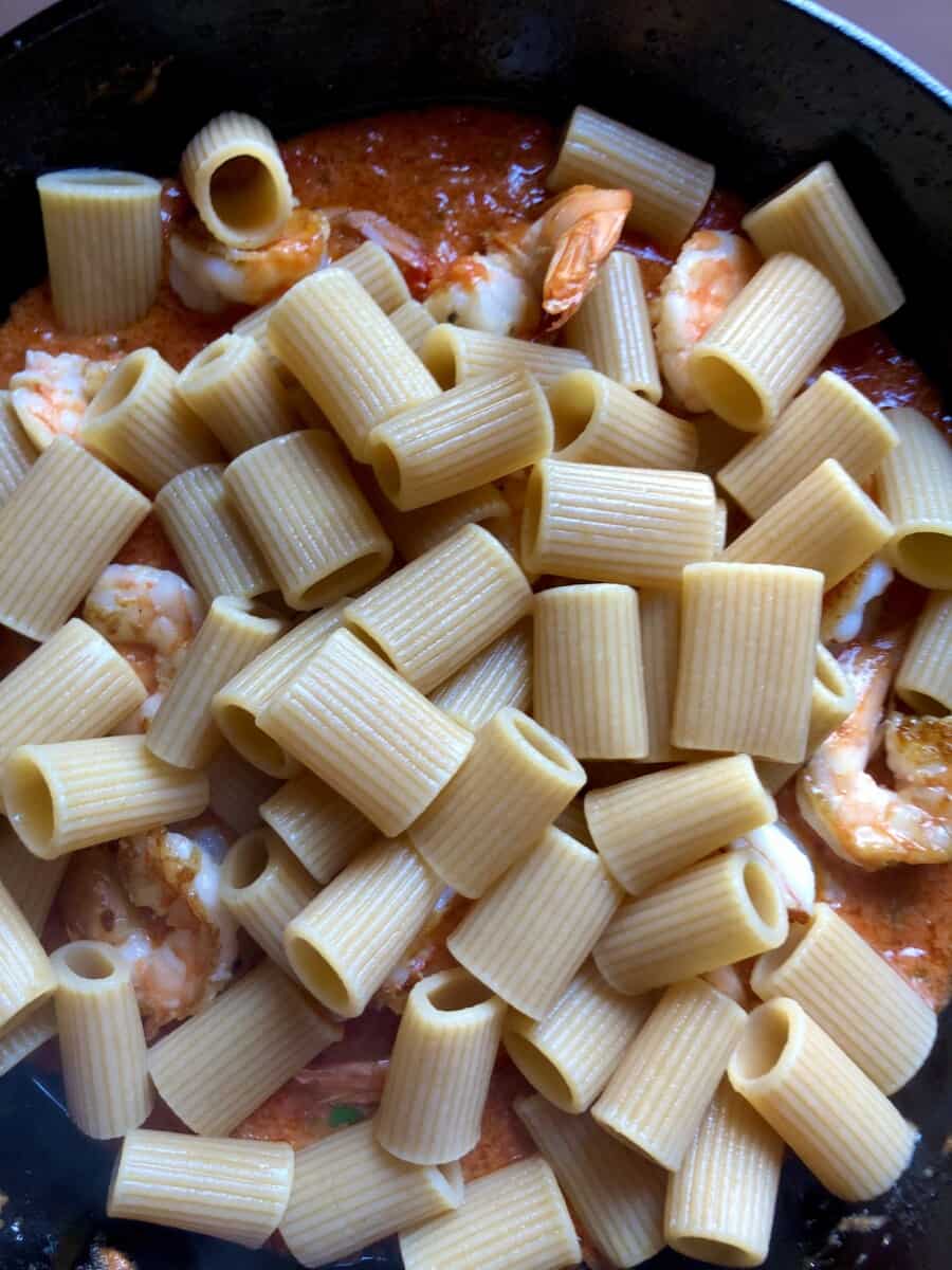 A cast iron pan filled with tomato alfredo pasta (pink sauce) with the rigatoni noodles not yet tossed together with the sauce.