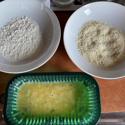 breading station with egg wash, flour, and panko bread crumbs in separate bowls and containers