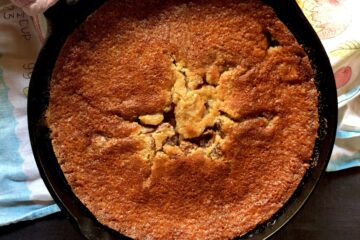 a cast iron skillet with a golden brown cherry cobbler baked beautifully and the sunlight hitting it