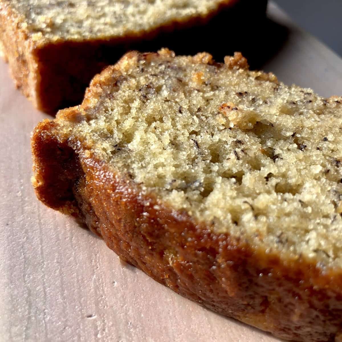 A slice of moist banana bread on a pink marble tray next to the rest of the loaf, best banana bread recipe from scratch.
