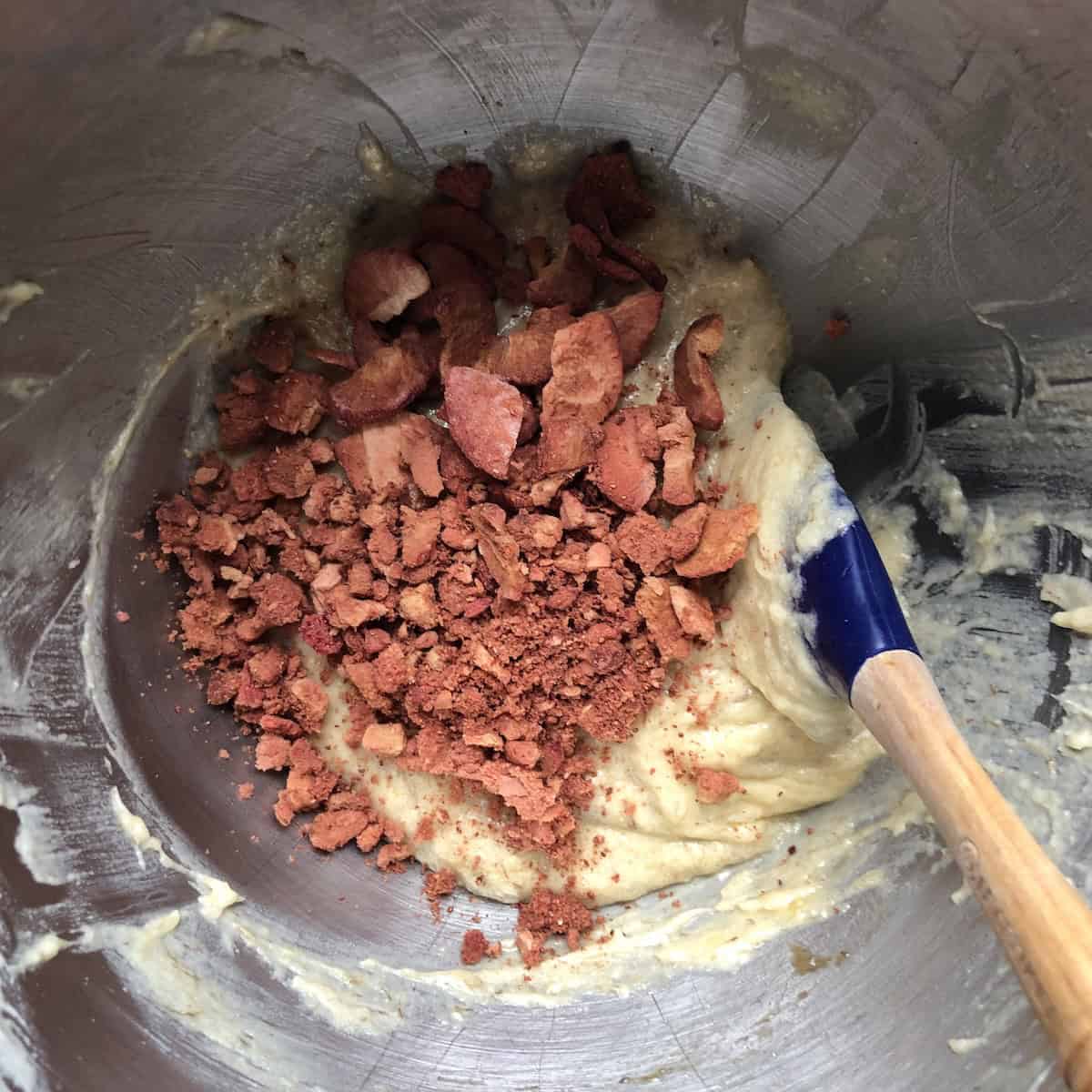Folding freeze-dried strawberry pieces into banana bread batter with a spatula.
