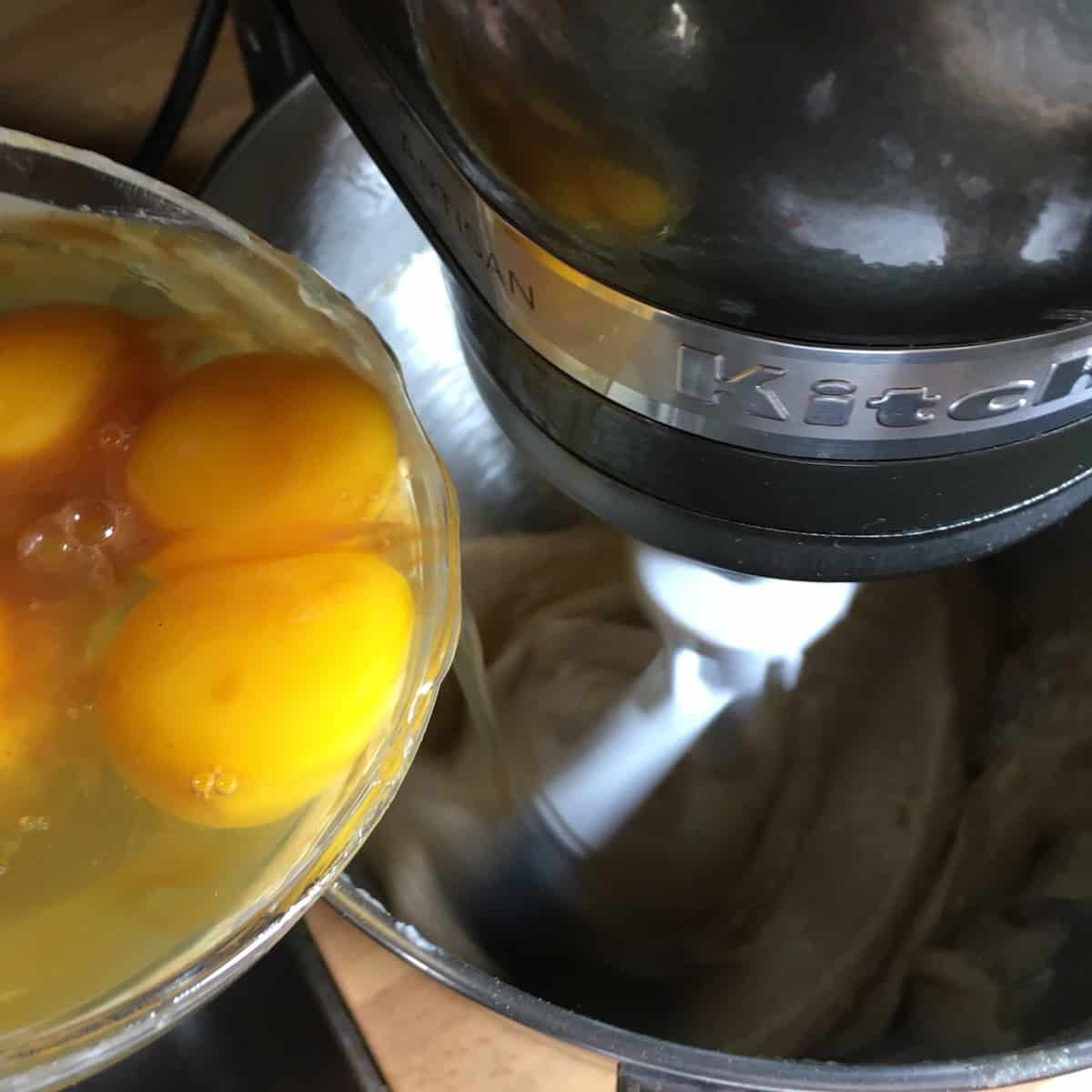 Eggs added one at a time to the flour and butter sugar mixture in a stand mixer bowl for the best carrot cake recipe.
