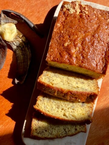 An overripe exposed banana next to the most moist banana bread loaf that's partially sliced.