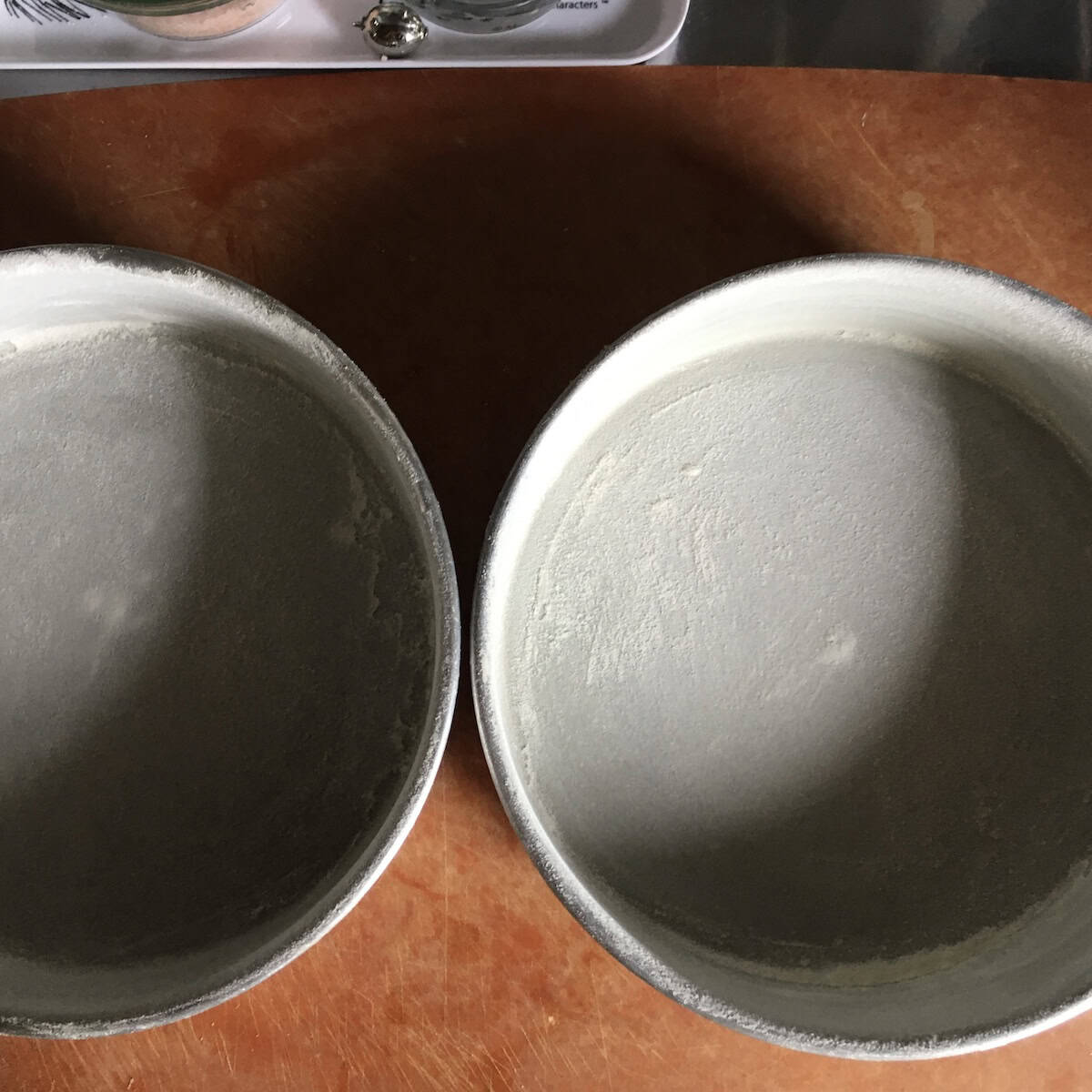 Two buttered and floured 8-inch cake pans ready to fill with batter for a double layer carrot cake recipe from scratch.