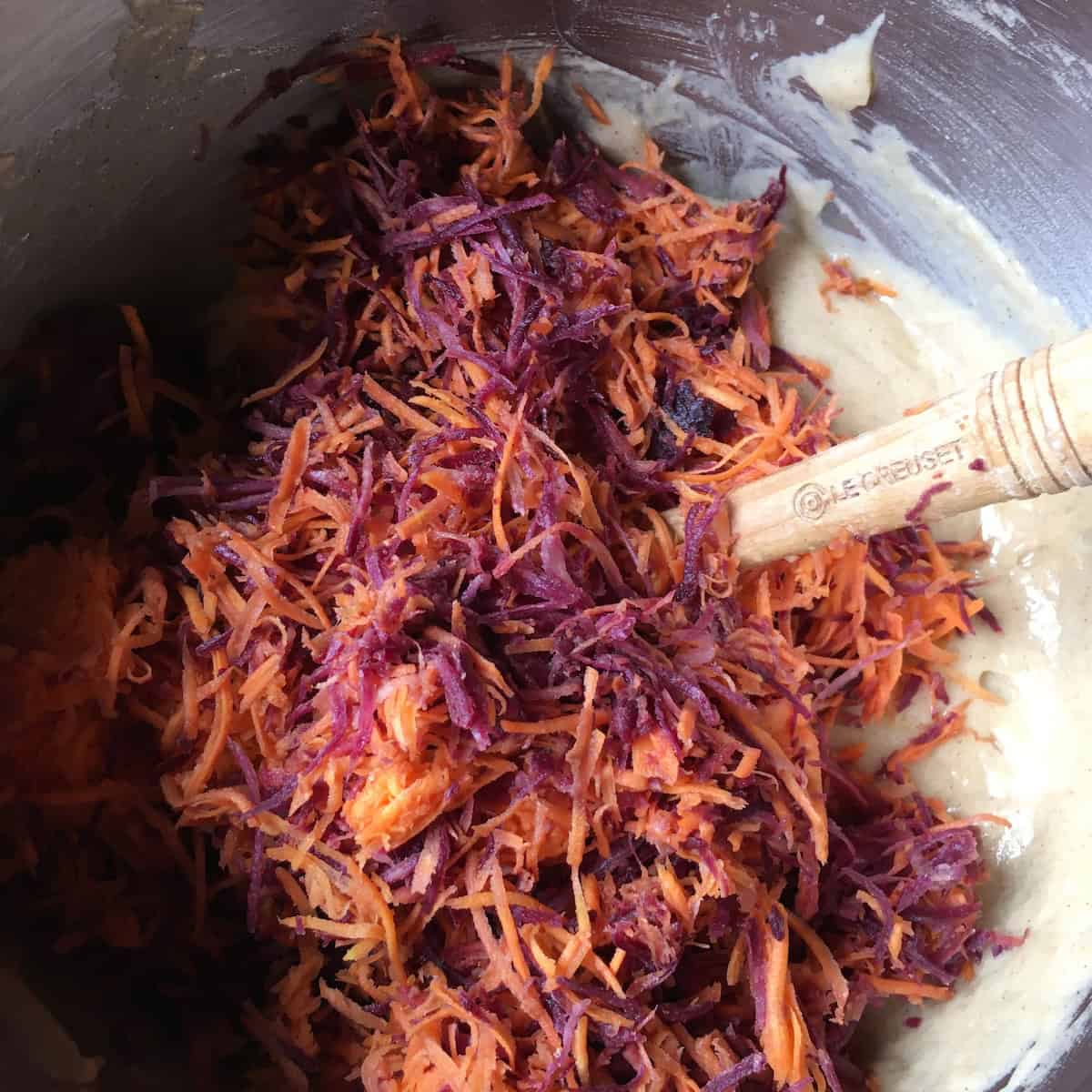 Freshly shredded carrots added to the carrot cake batter in a stand mixer bowl, ready to be folded in for a homemade carrot cake recipe from scratch.