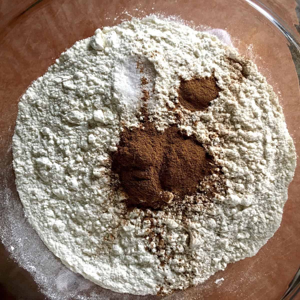 Measured dry ingredients in a mixing bowl for an easy carrot cake recipe from scratch, including flour, cinnamon, salt, and baking soda.