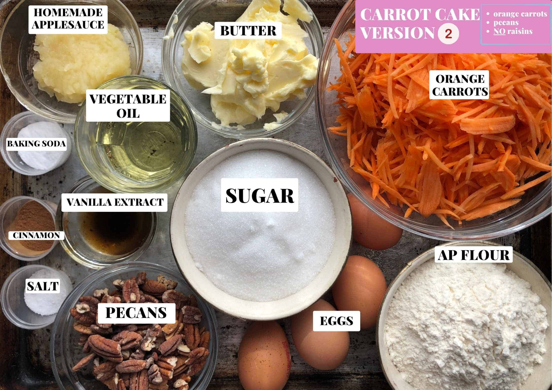Labeled carrot cake ingredients for Version 2 on a cutting board with orange carrots and toasted pecans and no raisins, a simple easy carrot cake for anyone who prefers their carrot cake without raisins.