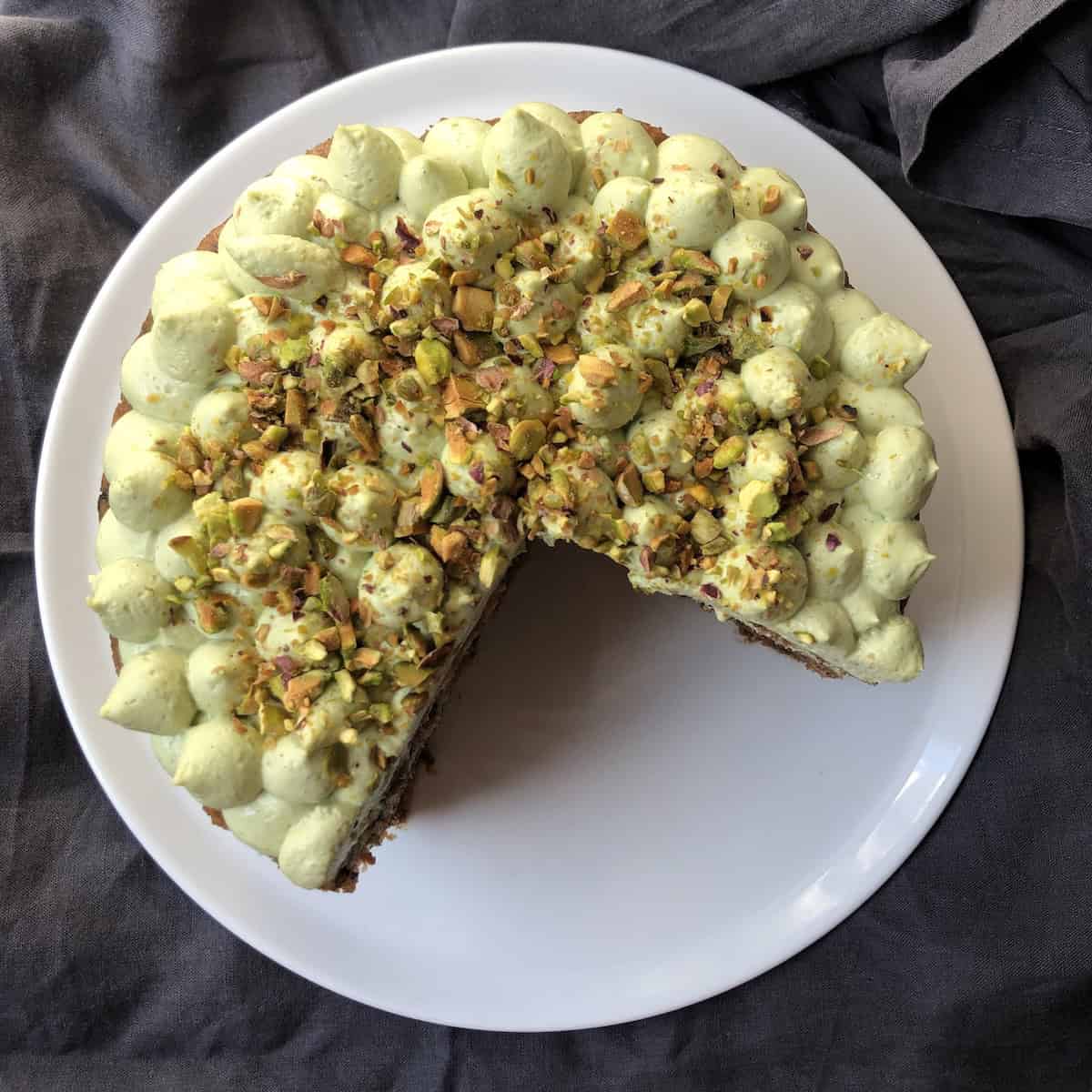An orange carrot cake with pecans and matcha cream cheese mascarpone frosting with a slice removed, showing a super moist crumb with no raisins showing the world's best carrot cake!