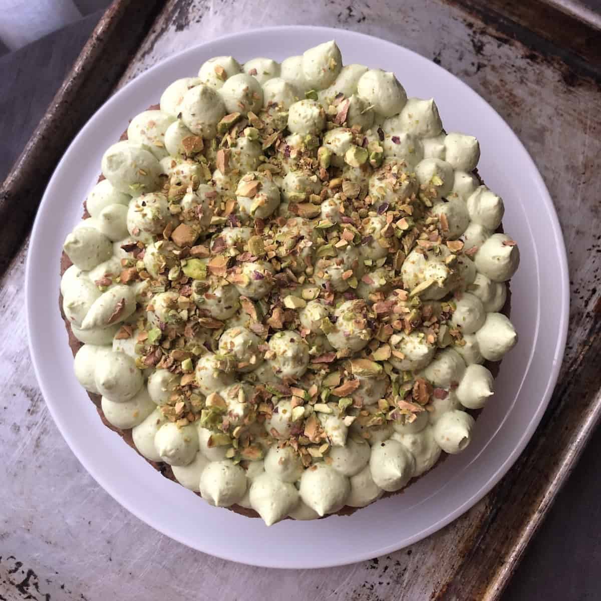 An orange carrot cake with pecans fully covered in matcha cream cheese mascarpone frosting and garnished with toasted chopped pistachios for color, flavor, and texture showing the best carrot cake ever with or without pineapple, and just as stunning turned into cupcakes or carrot cake muffins.