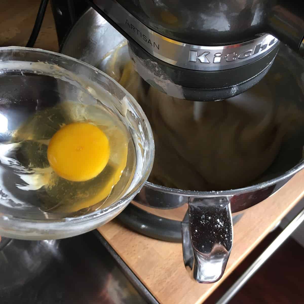 The last egg being added to the carrot cake batter in a stand mixer bowl before the final flour mixture is incorporated.

